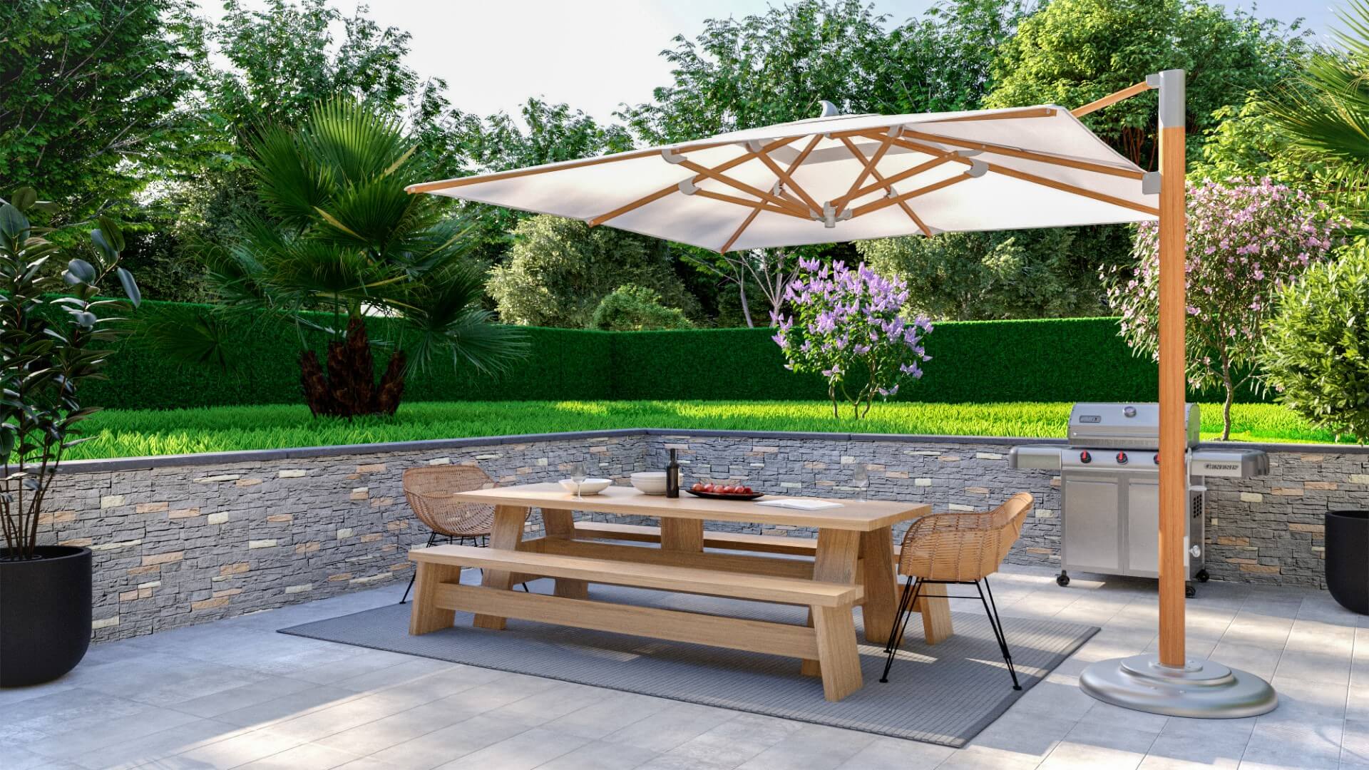 Modern outdoor dining area with a large wooden picnic table, wicker chairs, and a large umbrella, set on a tiled patio with a faux rock panel stone ledge wall, surrounded by lush greenery and a built-in barbecue grill.