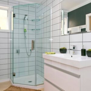 A bathroom with white tile-patterned wet wall panels on the wall, a glass-enclosed corner shower, and a white vanity with a mirror above it.