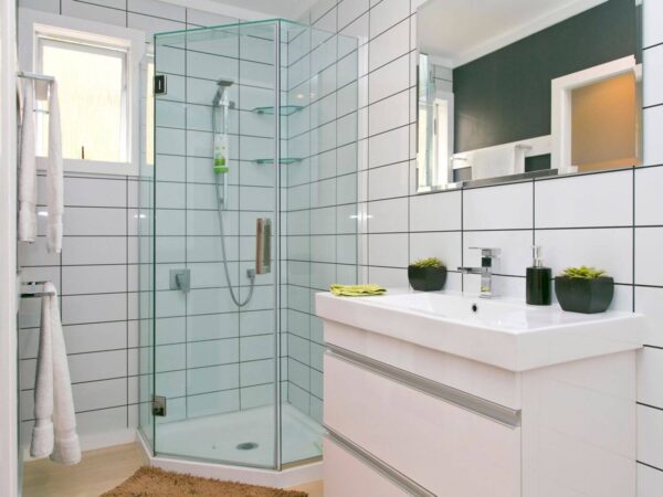 A bathroom with white tile-patterned wet wall panels on the wall, a glass-enclosed corner shower, and a white vanity with a mirror above it.