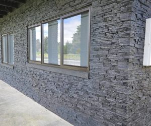 House exterior with black ledge stone over cladding, featuring large windows and a concrete walkway.