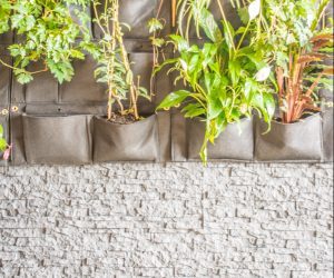 A vertical garden with green plants growing in fabric wall pockets, mounted above a white stacked stone wall.