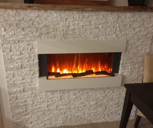 An electric fireplace with a white stacked stone surround and wooden mantle piece.